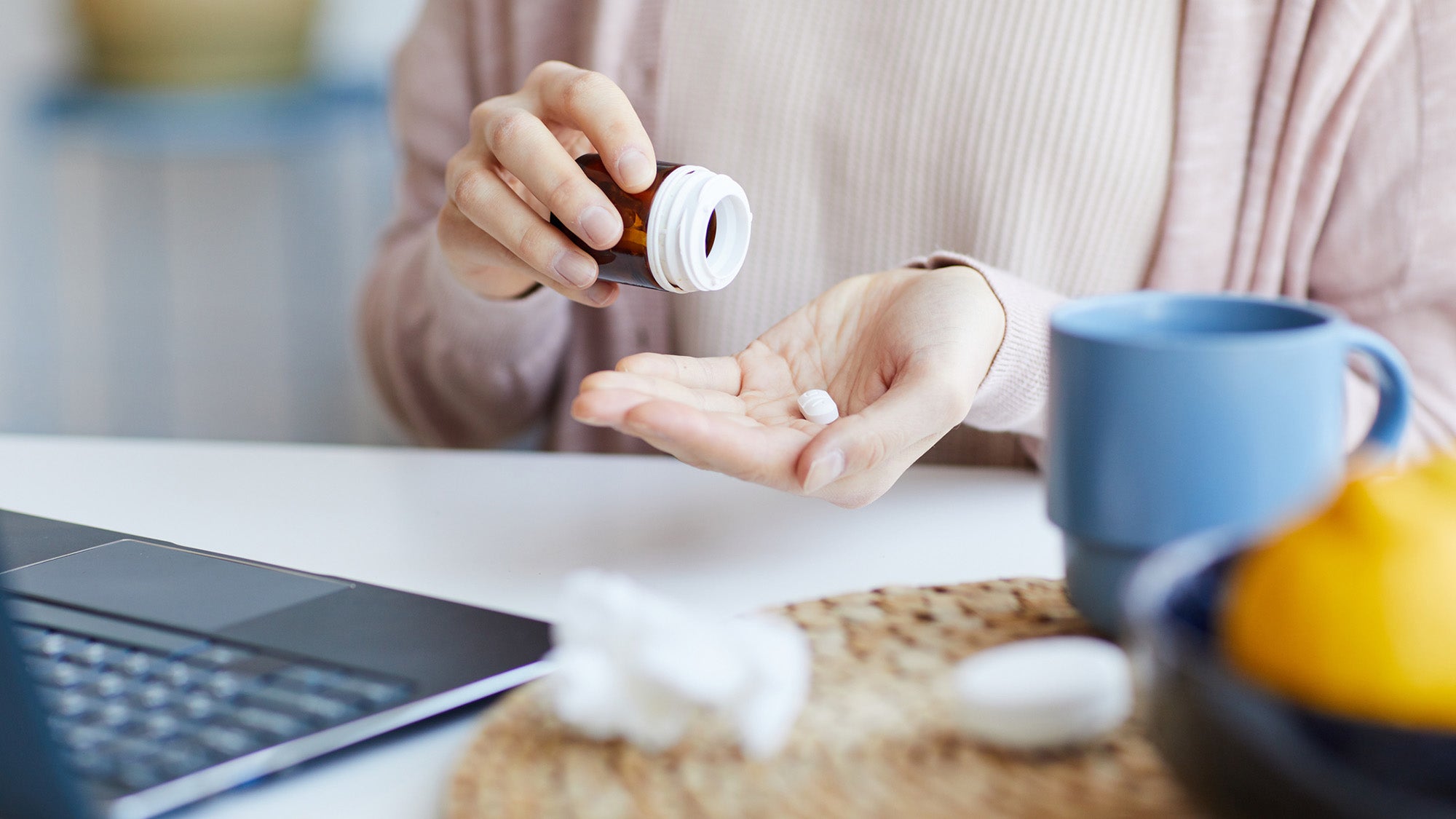Close-up of woman sitting at the table with laptop and pill bottle
