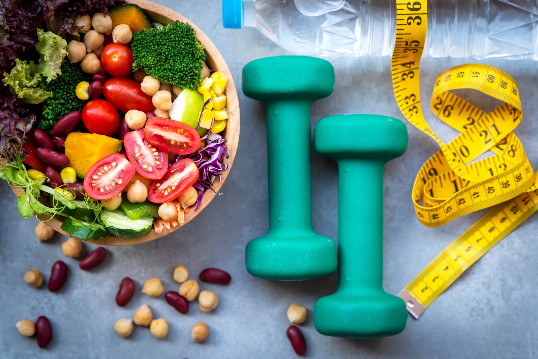 Top view of a salad, bottle of water, hand weights, and a soft tape measurer