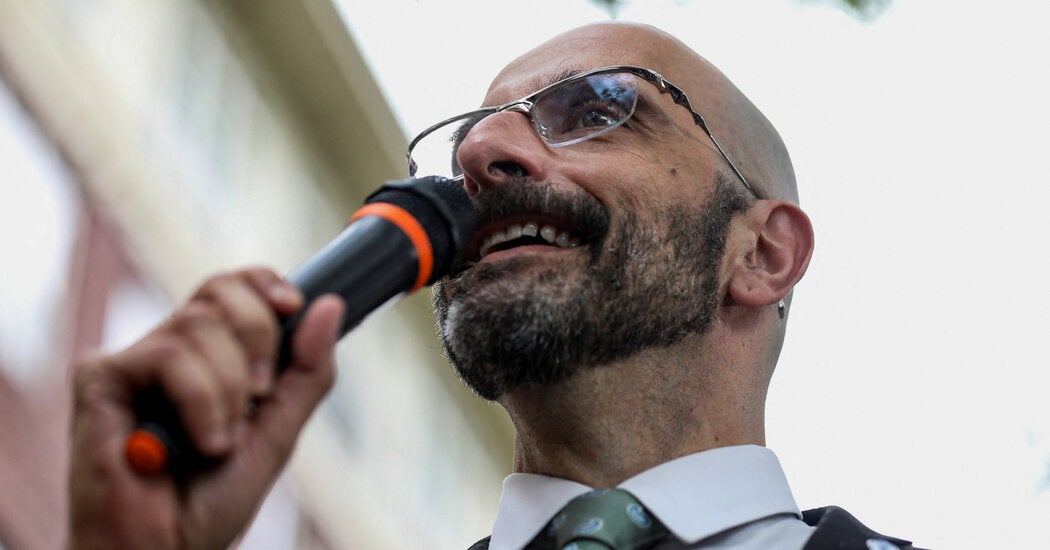 Demetre Daskalakis using handheld mic at event.