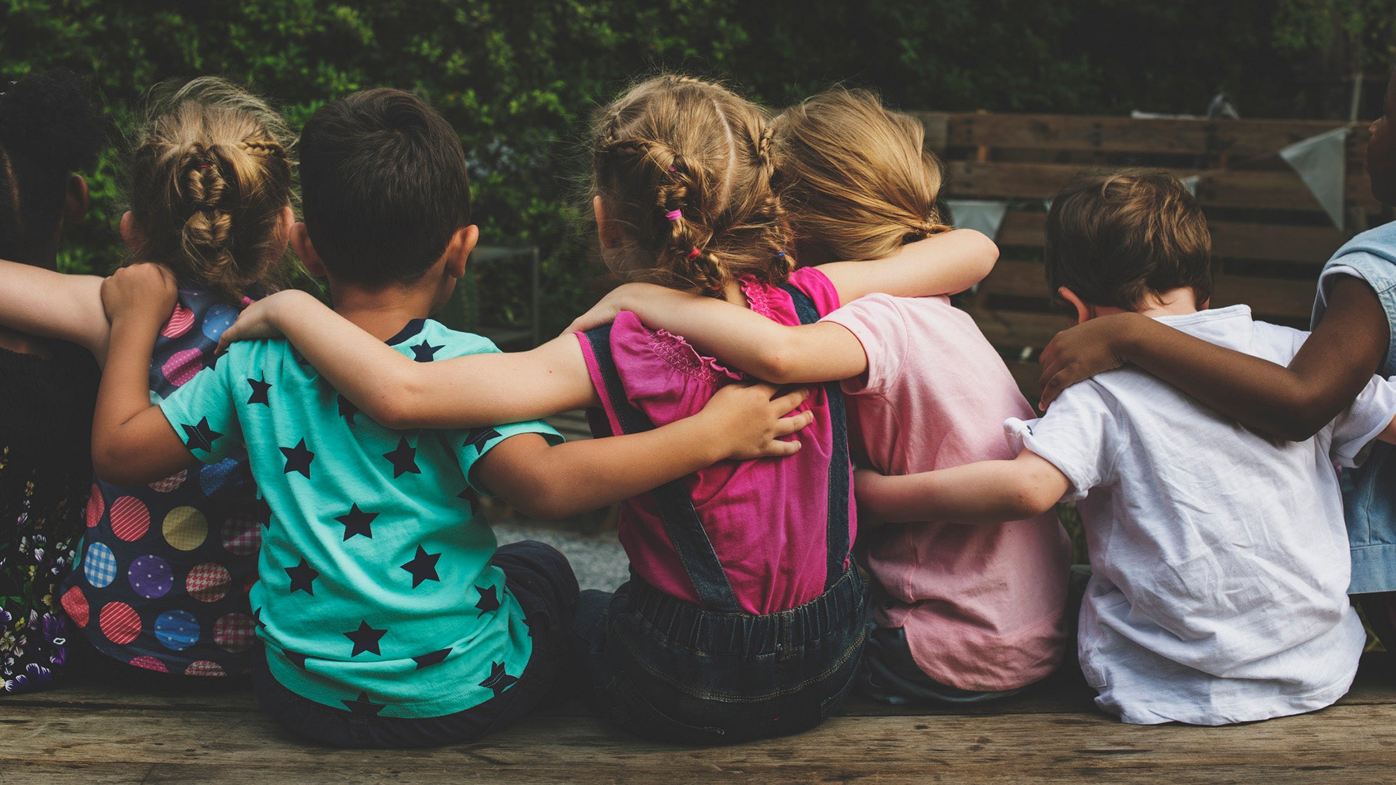 Group of children sitting with their arms around each other, from rear
