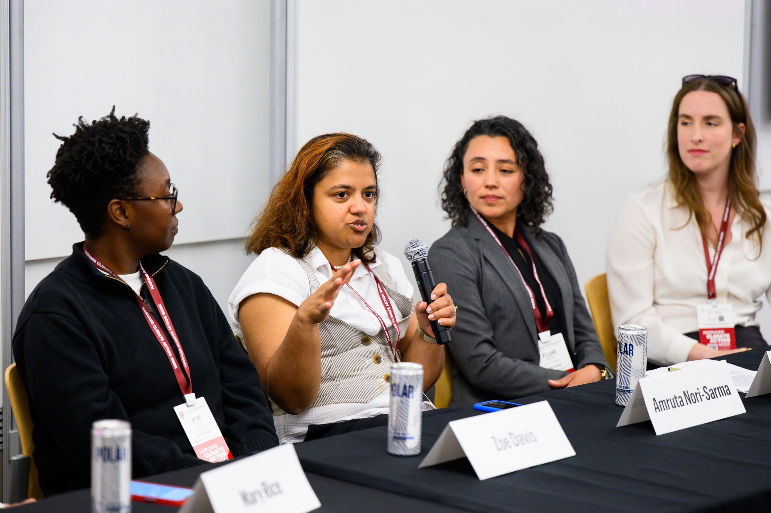 Zoe Davis, Amruta Nori-Sarma, Flor Amaya, and Anne Coglianese sit at a table. Nori-Sarma, second from left, speaks into microphone.