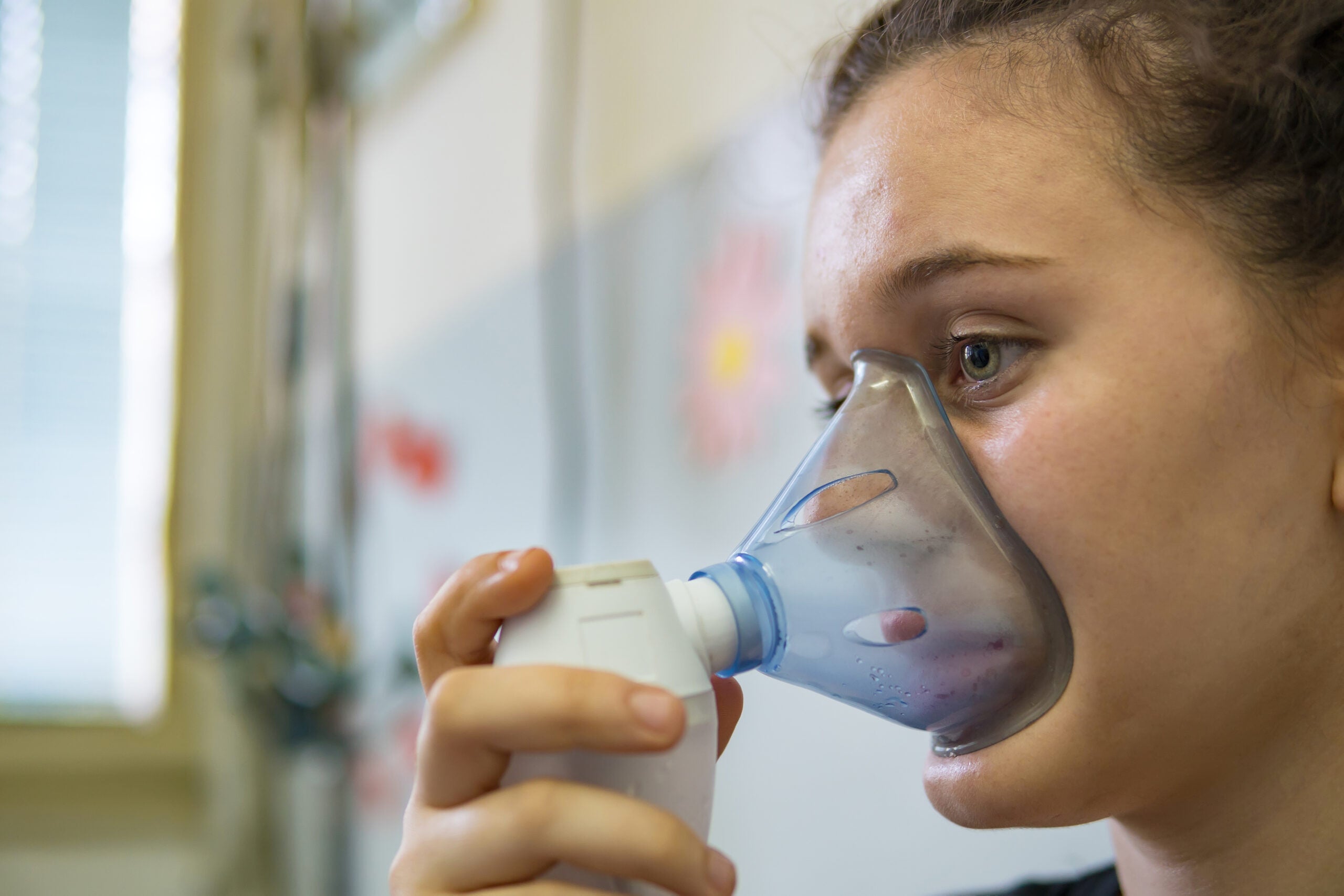 A young woman using a bronchodilator to treat respiratory symptoms at the emergency room of the hospital.