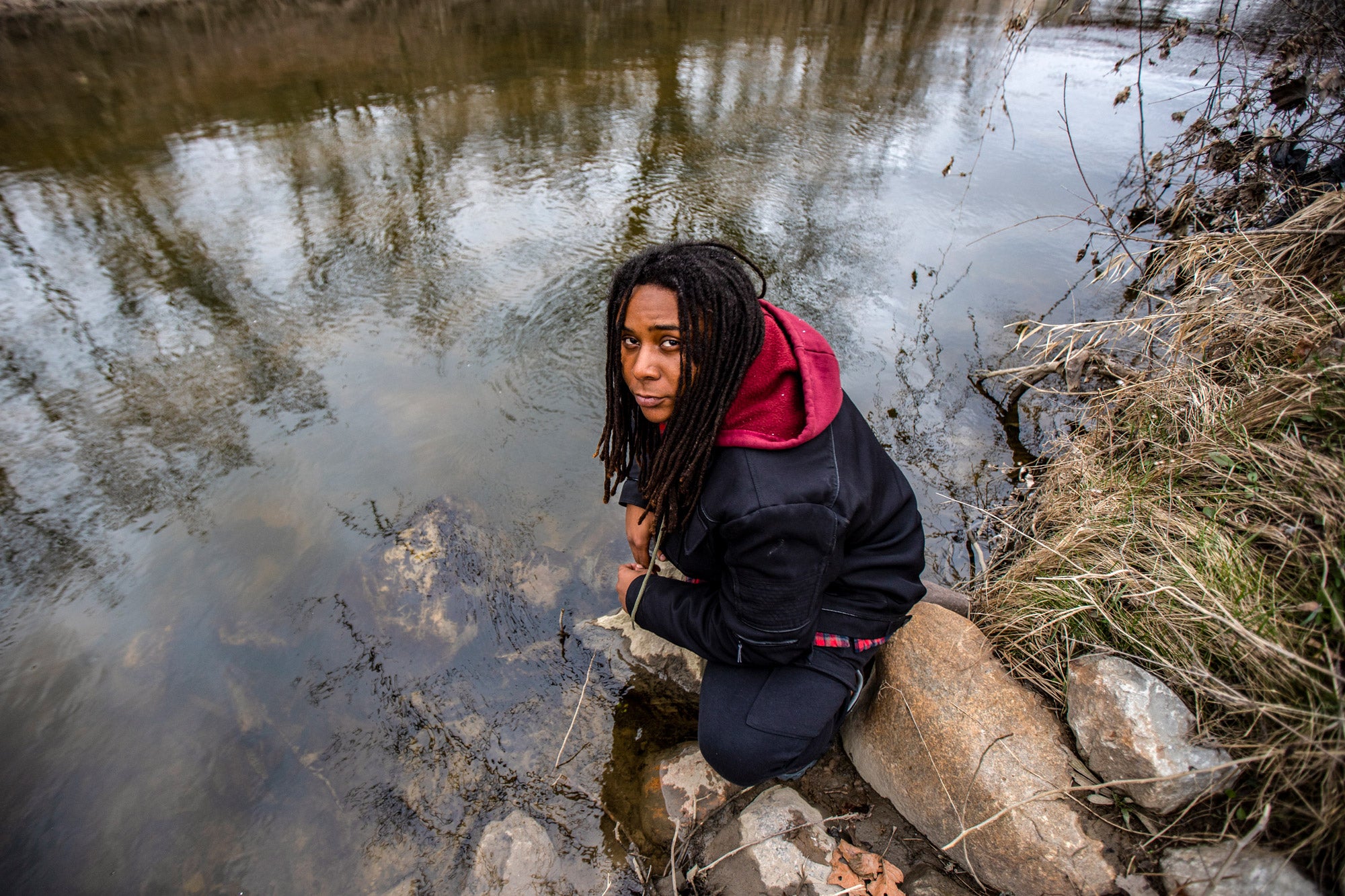 Marcel Simmons squats on some rocks near the edge of the Flint River. He stares somberly up at the camera.