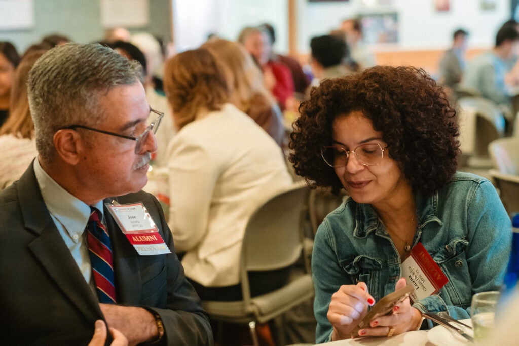 Alumni at a table discuss something one is showing the other. 