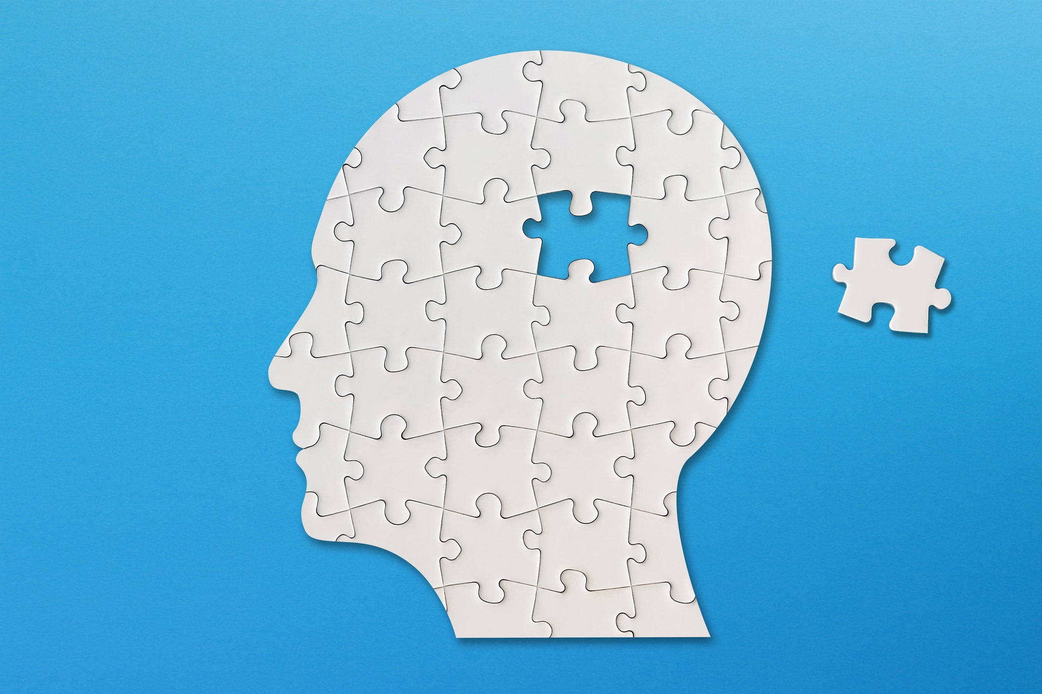 Brain shaped white jigsaw puzzle on blue background, a missing piece of the brain puzzle
