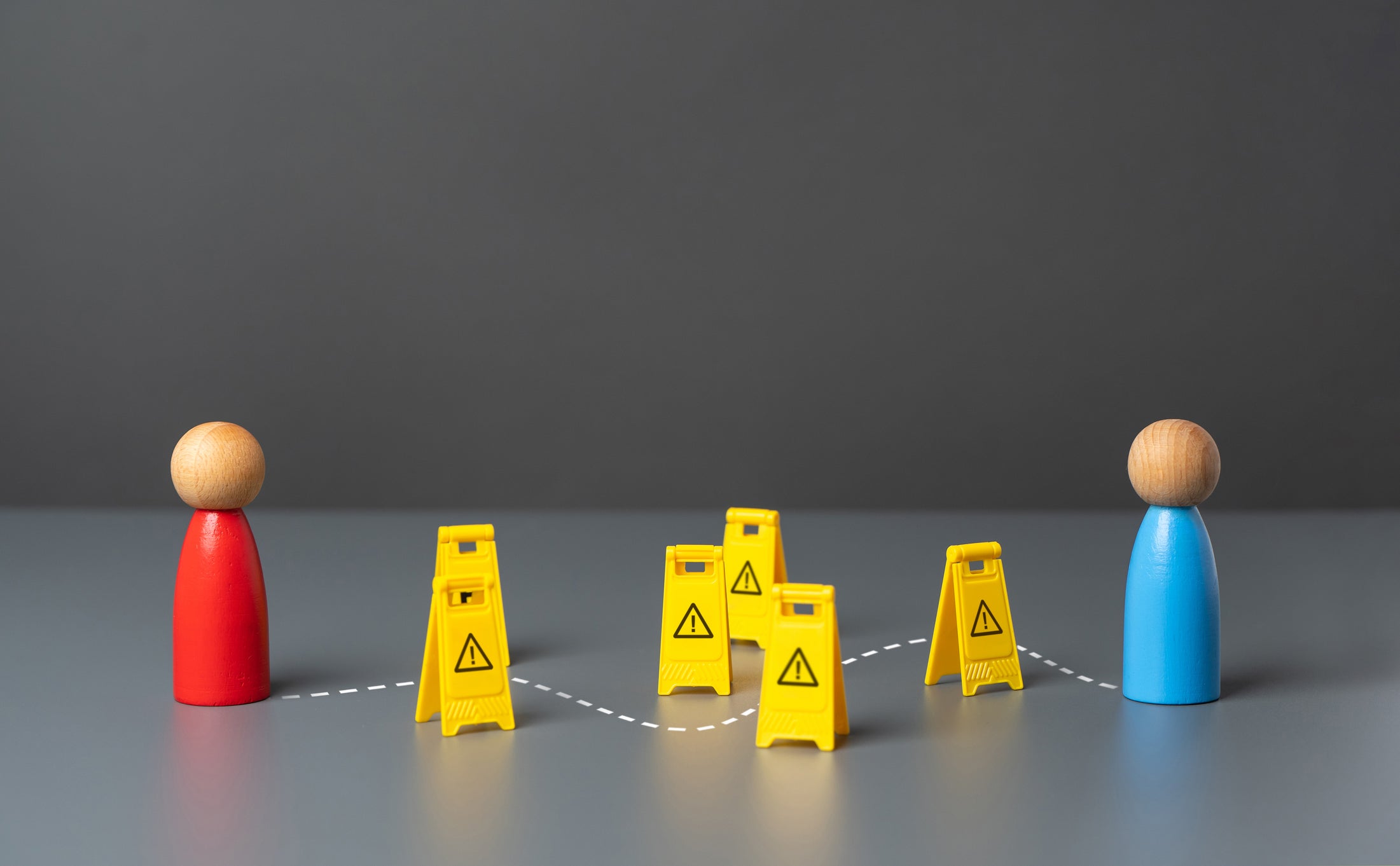 A red figurine and a blue figurine face each other with caution symbols dotting the winding path between them.