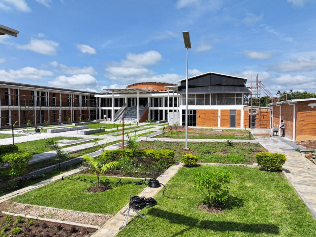 A steel, white and wood series of buildings and green plots of grass and plants, part of the ACEGID campus in Ede, Nigeria.