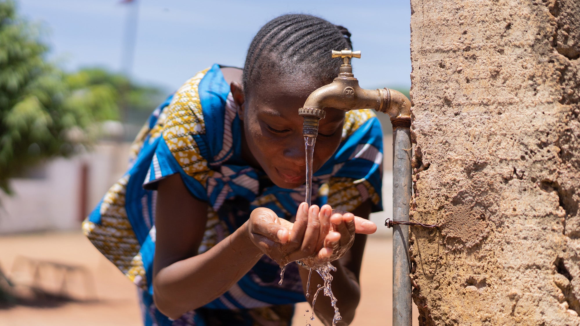 Girl drinking from water spigot in Bamako, Mali
