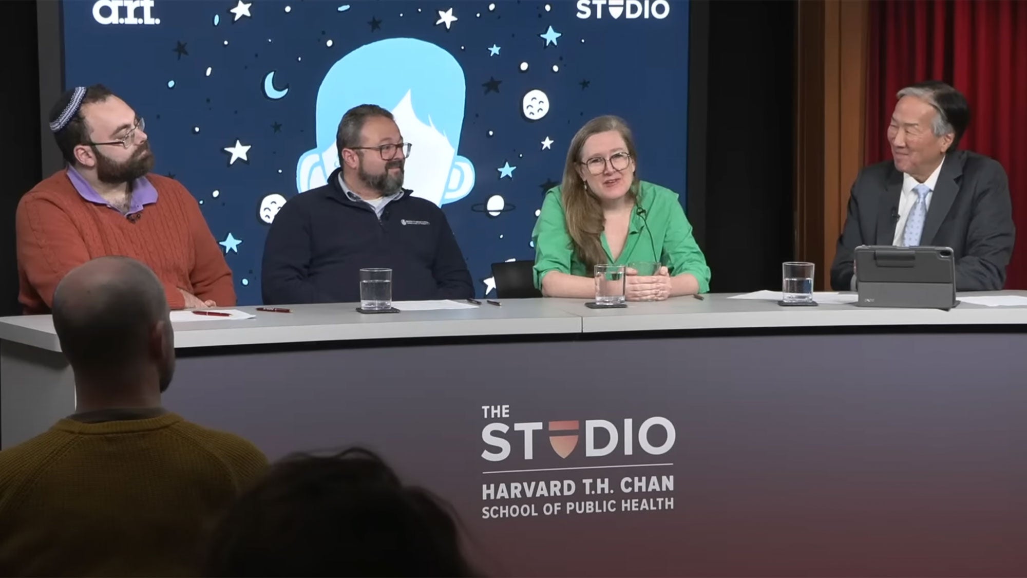 Ari Ne’eman, Jason Fogler, Sarah Ruhl, and Howard Koh sitting behind a desk on the Studio set.