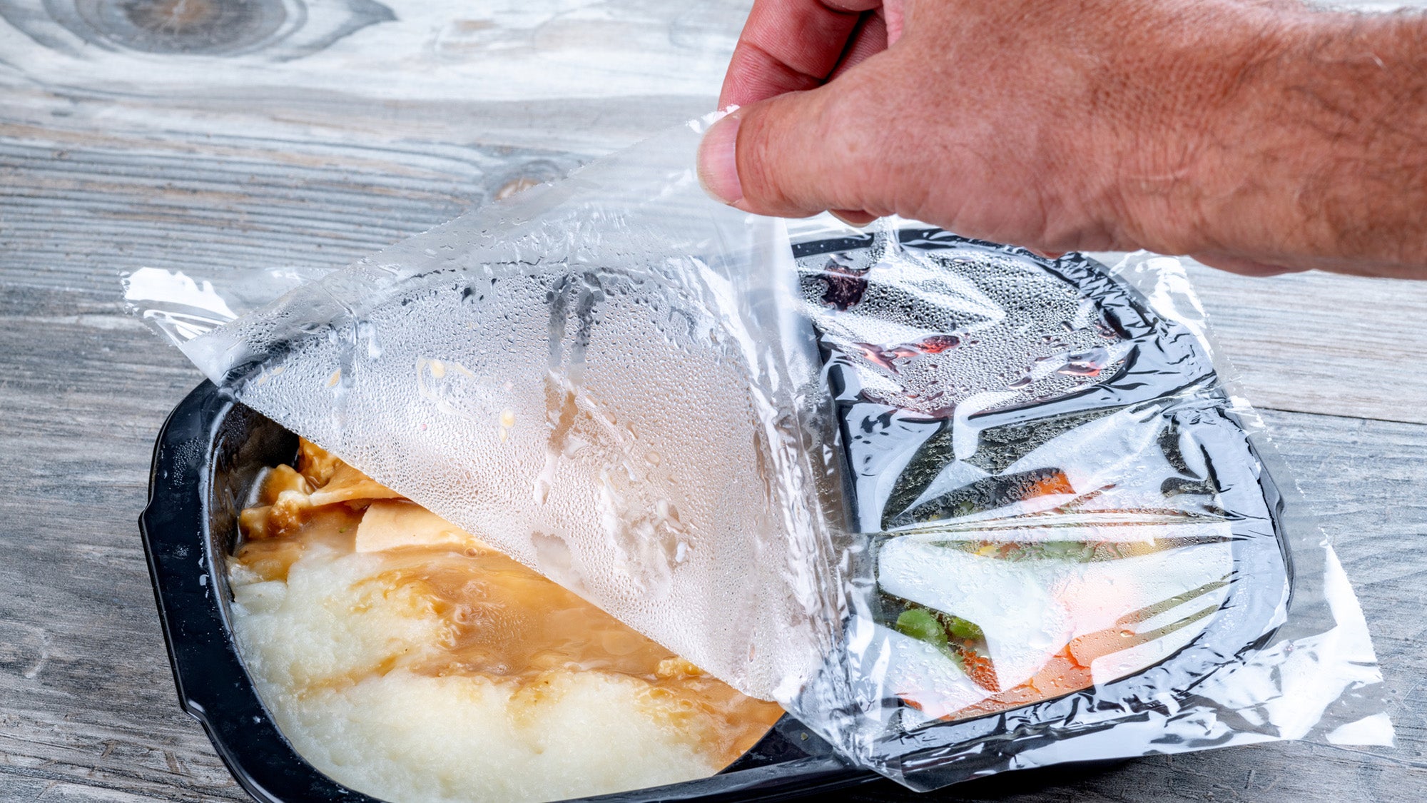 hand pulling back plastic film on microwave dinner