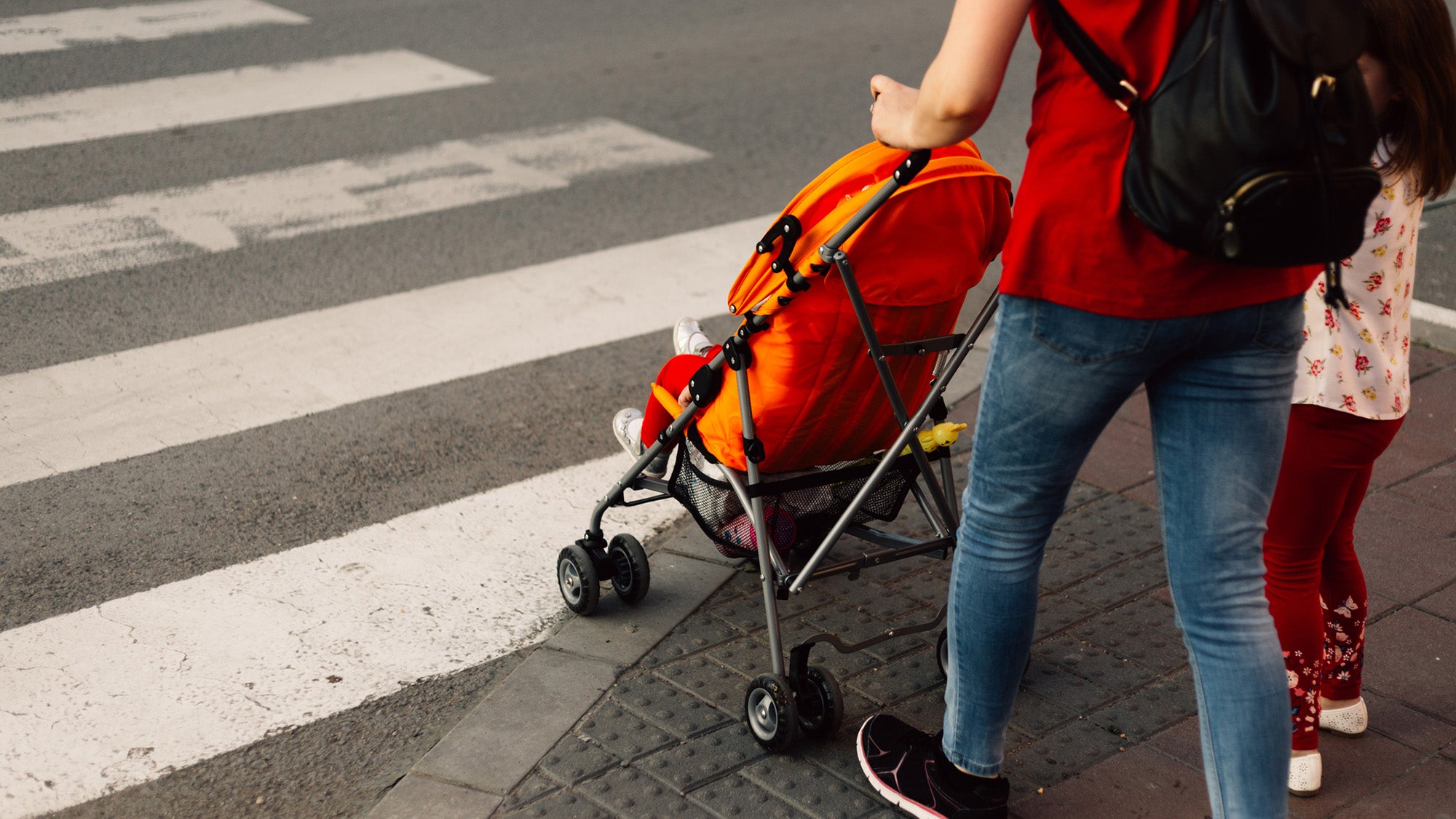 woman pushing baby in stroller and young girl stand by crosswalk