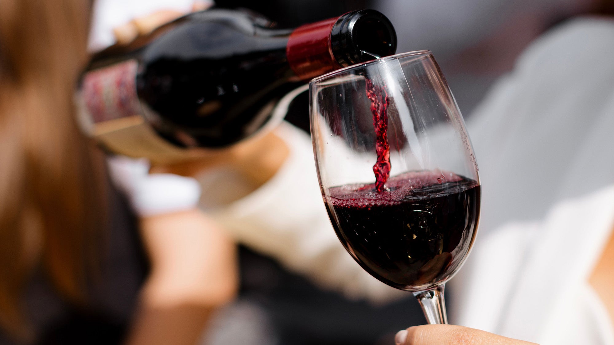 person pouring red wine into a glass