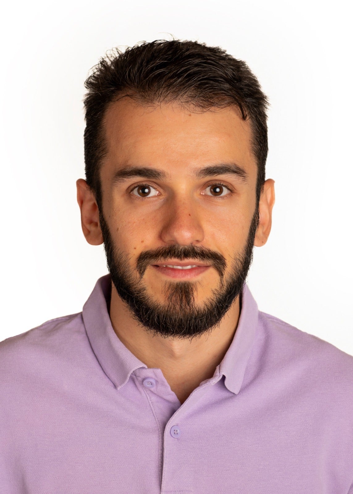a headshot of Dr. Joaquín Martínez-Minaya. He looks directly at the camera, and has short hair and a close-cropped beard and mustache. he wears a light purple collared shirt and the background is white