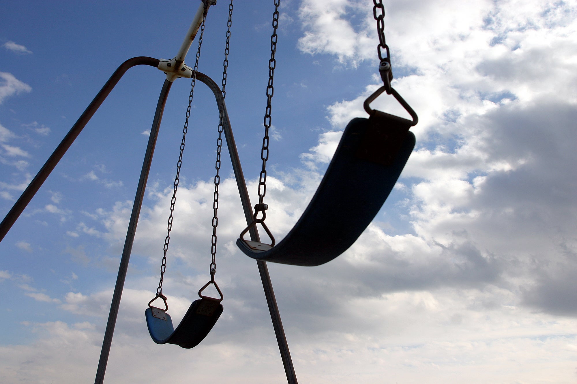 Silhouette of a swingset, shot from above, against a blue sky with clouds.