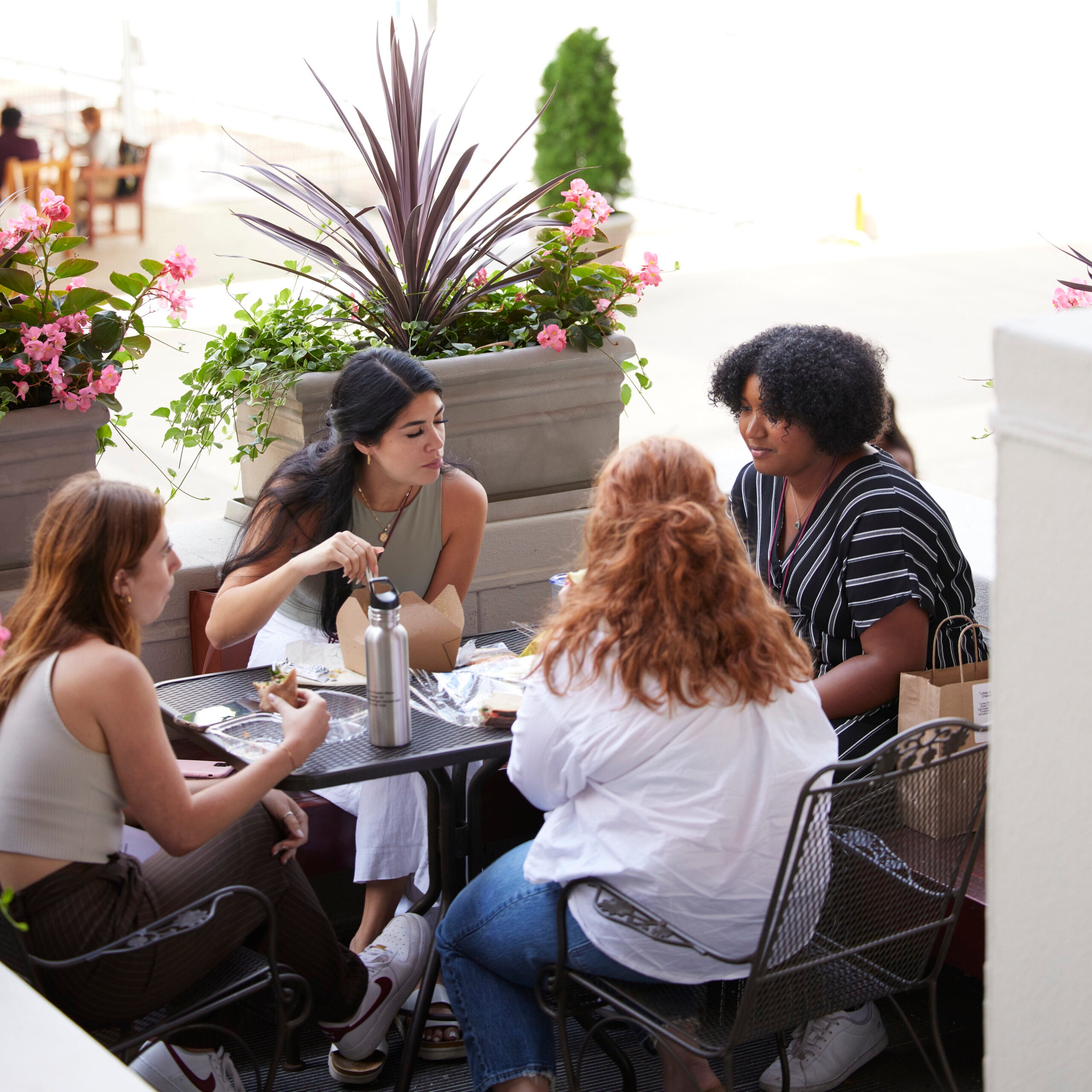 Four students enjoy lunch at a table outside Kresge surrounded by blooming planters. 