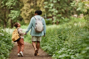 Back view of joyful mother and daughter walking on nature trail together holding hands