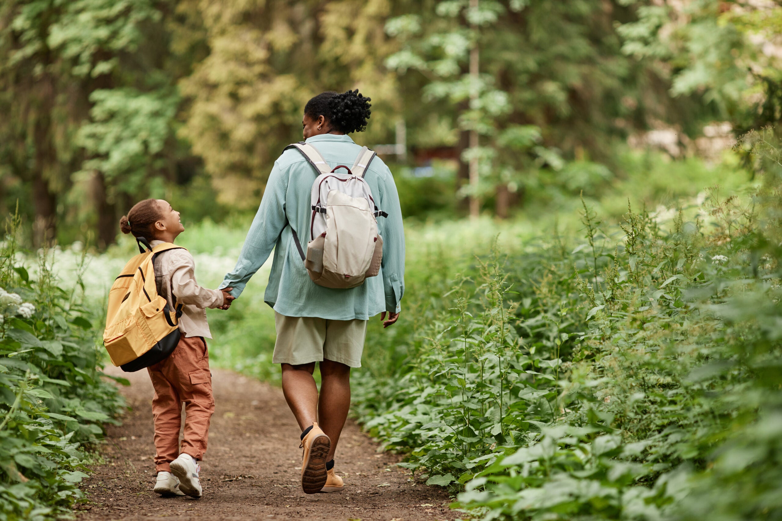 Back view of joyful mother and daughter walking on nature trail together holding hands
