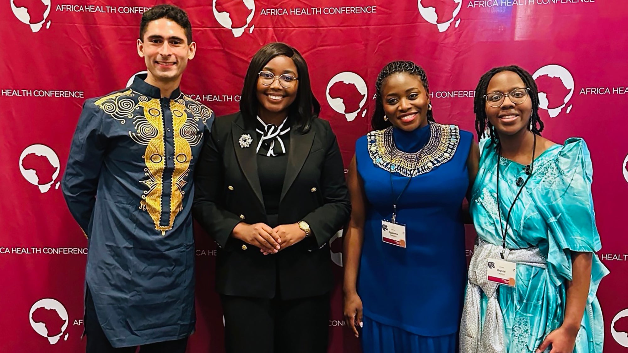 Four people pose in front of a backdrop with the conference logo