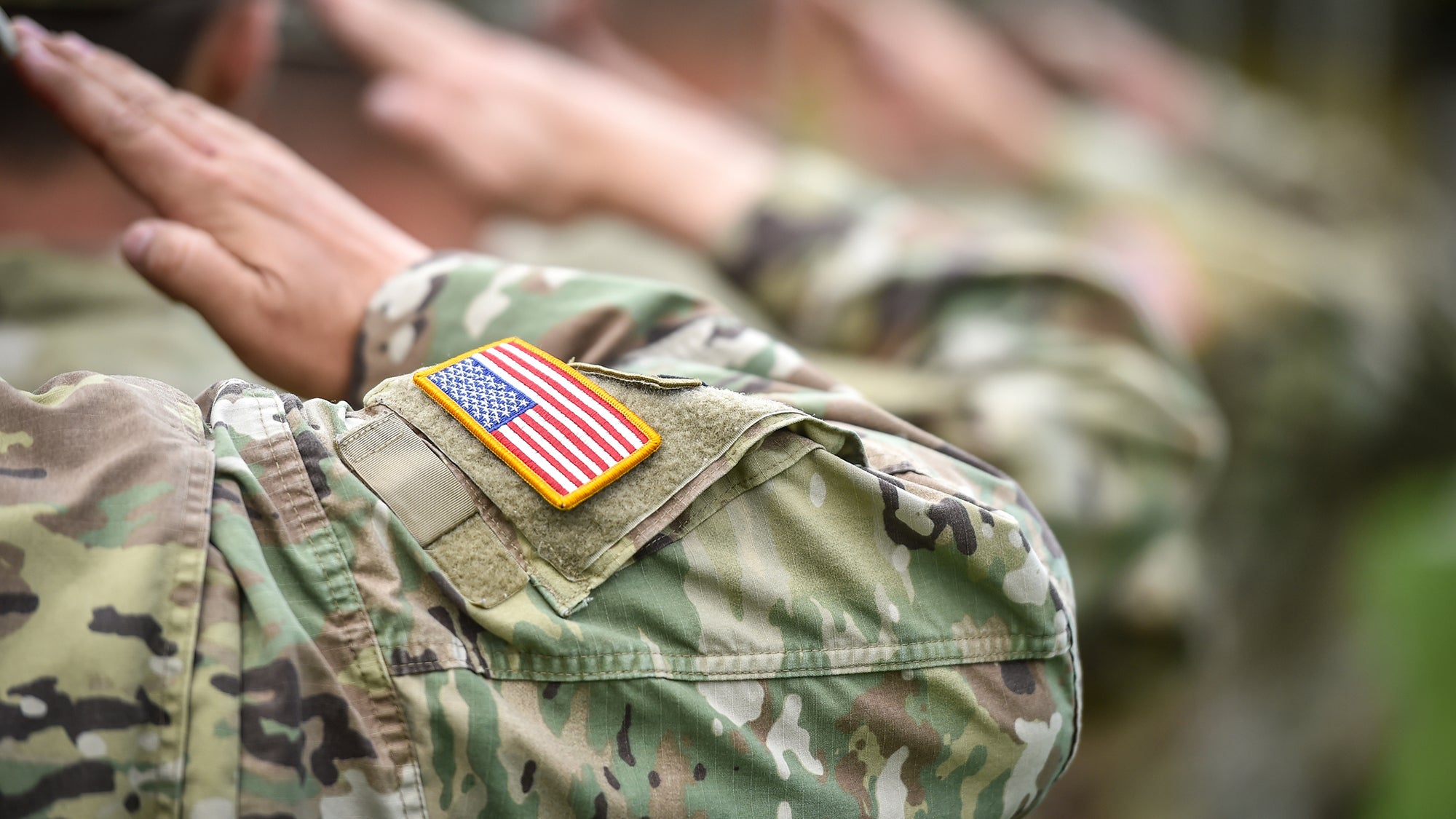 Military personnel giving the honor salute during military ceremony. American flag patch visible on arm of one soldier.