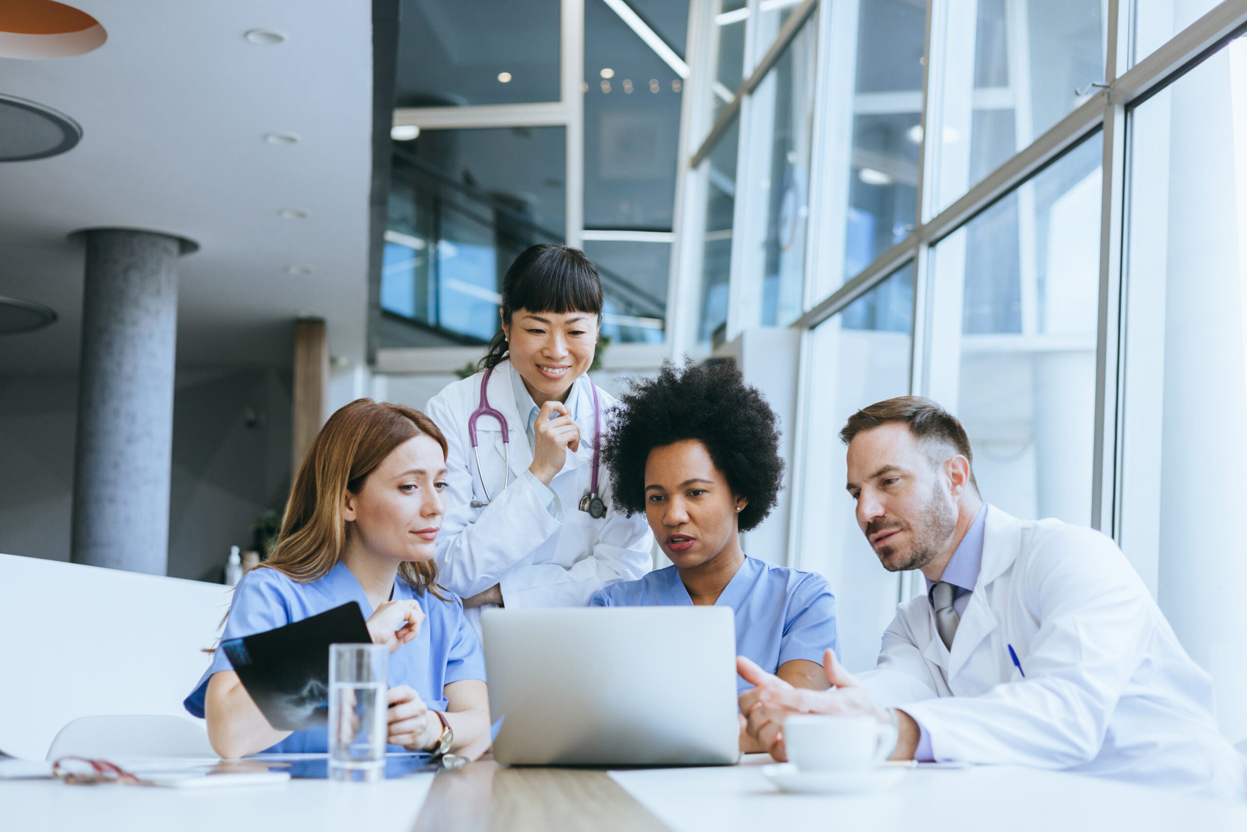 Doctors and nurses collaborate while looking at medical data on a laptop in a hospital meeting setting