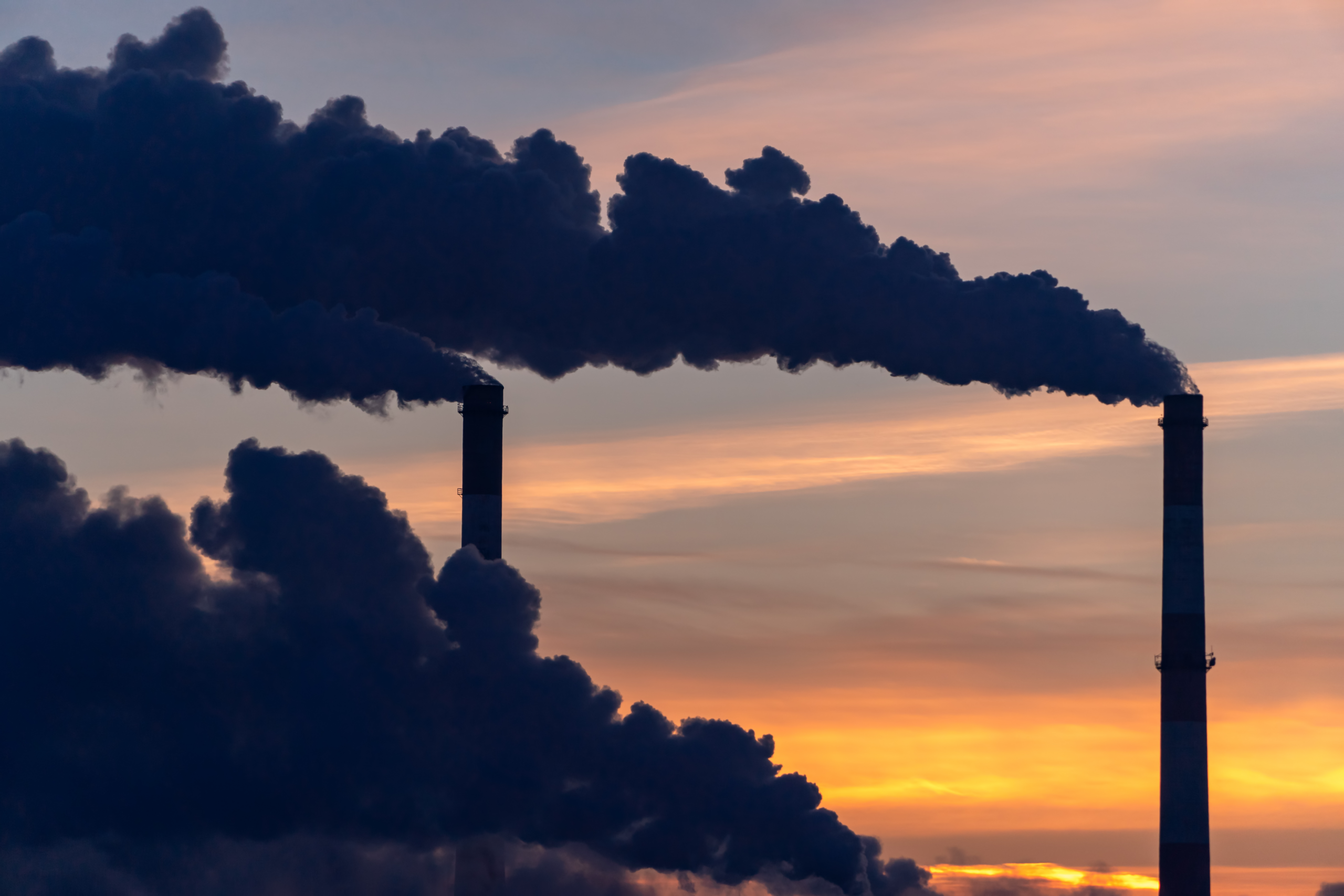 Two towers blowing smoke into the air at sunset