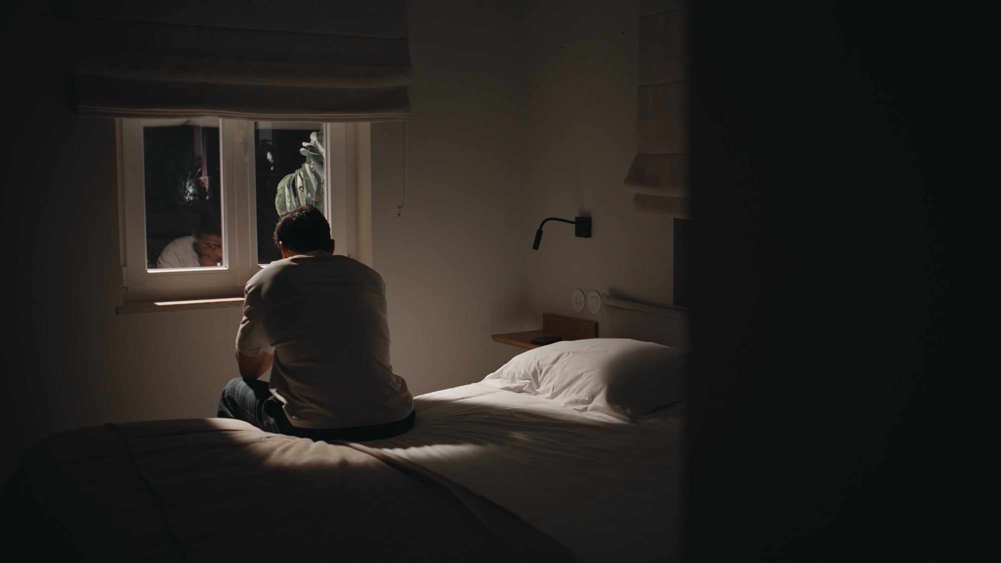 Man sitting on bed in dark, light coming in through window