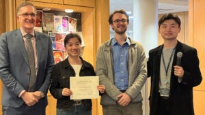 Three men pose with a woman holding an award certificate