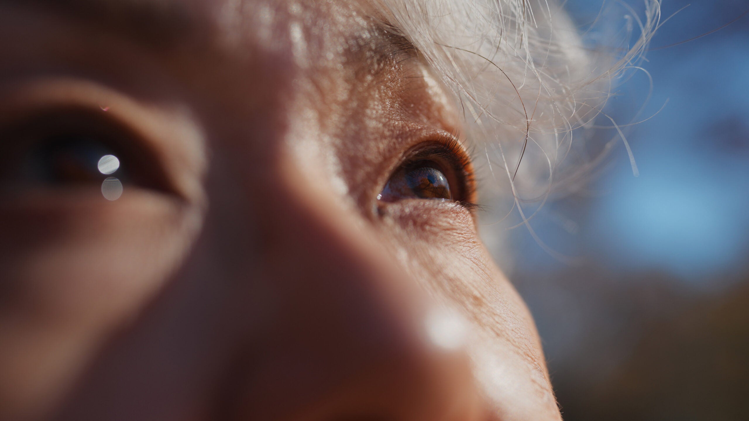 Close-up of older woman's eyes looking off into the distance. The sun shines on her face.