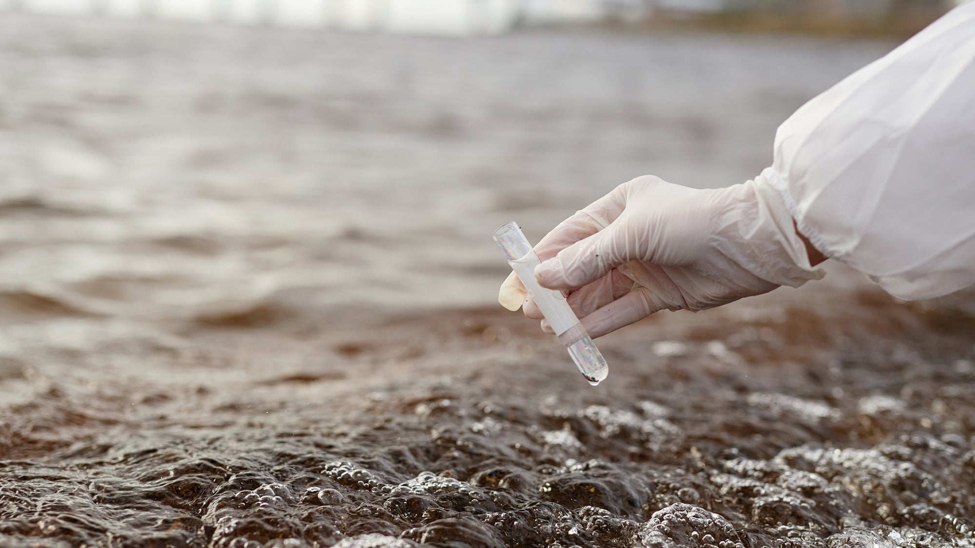 Close up of a hand with a test tube over water