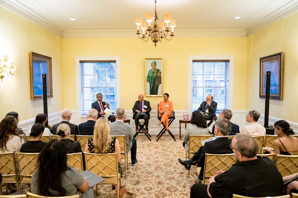 Three rows of audience members seated in gold chairs listen intently as India Research Center Director Vish Viswanath answers a question. He is seated at the front of the room with moderator Anthony Dias to the left, and fellow panelists and Harvard Chan faculty members Shruthi Mahalingaiah and Wafaie Fawzi on the right.