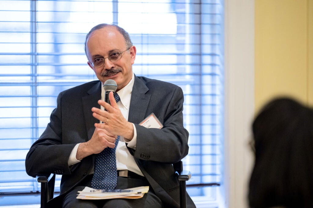 Wafaie Fawzi, seated in front of a window, speaks into a microphone held in his right hand.