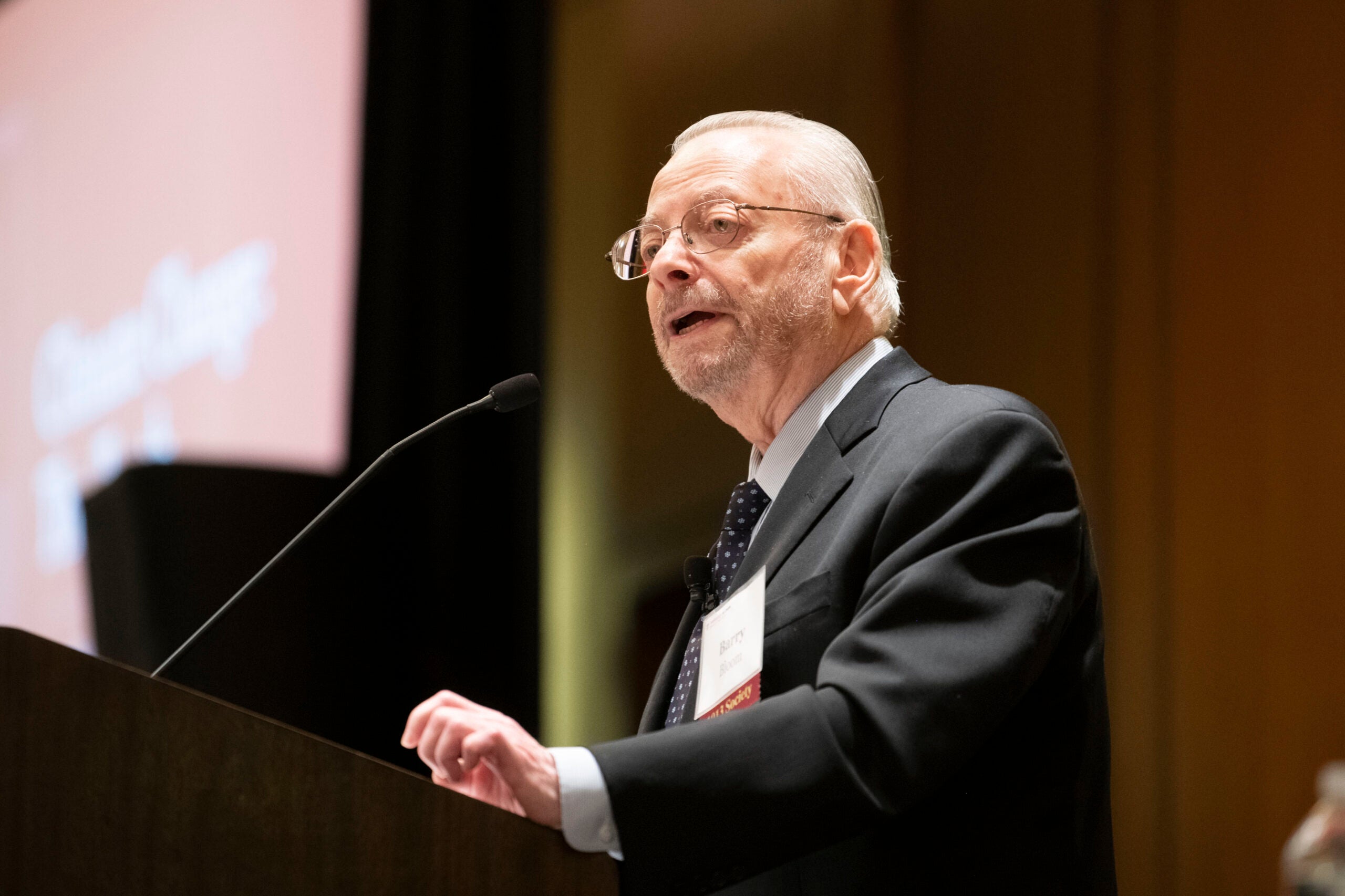 Dr. Barry Bloom speaking at a lectern, wearing a black suit.