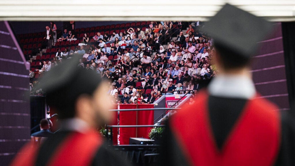 A view of the audience from behind two graduates
