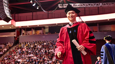 A graduate walks off the stage holding scroll
