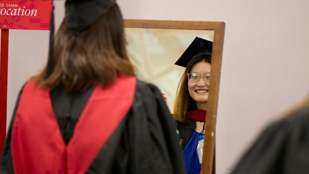 A smiling graduate looks in the mirror