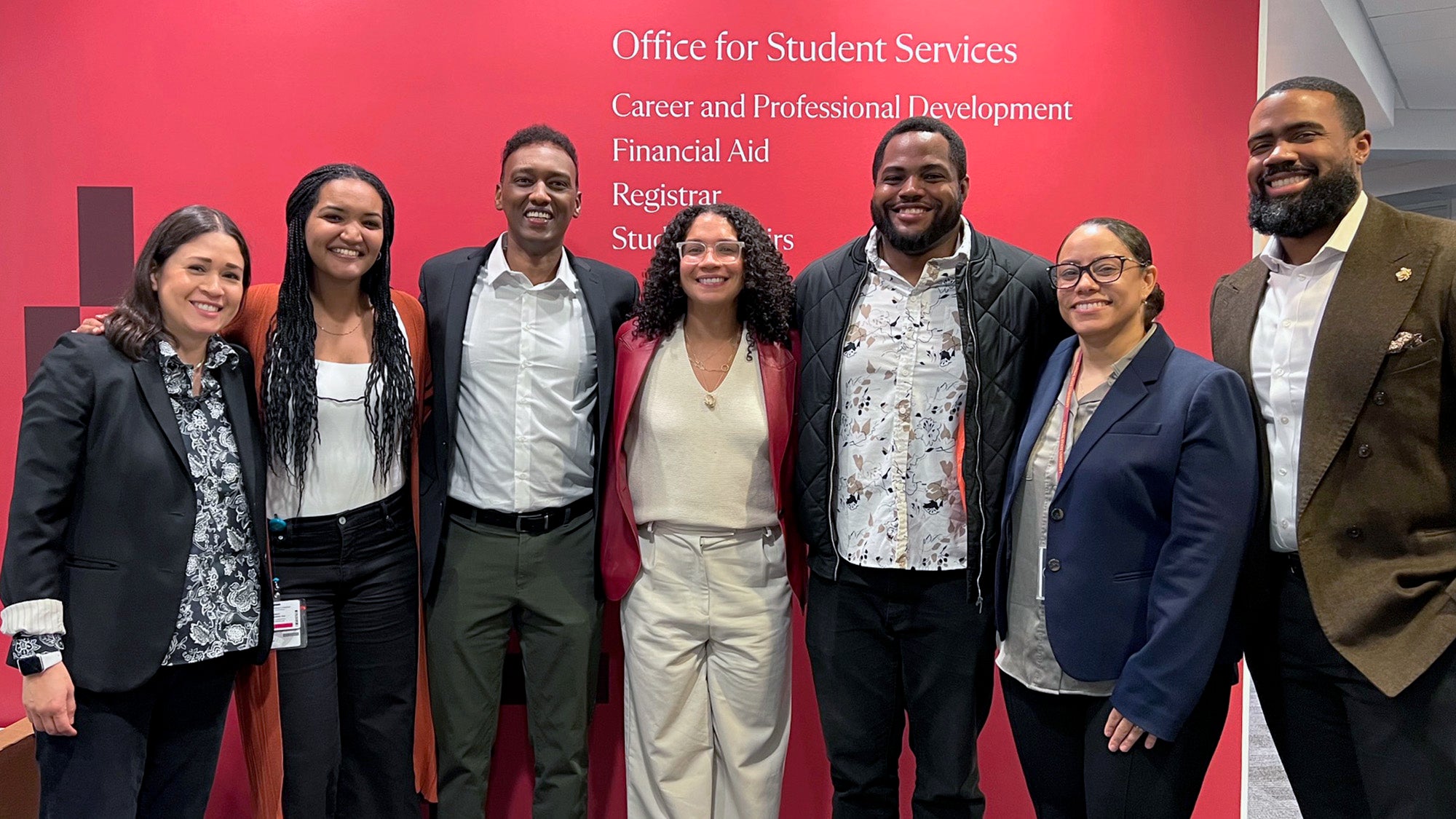 Seven people standing in front of a red wall