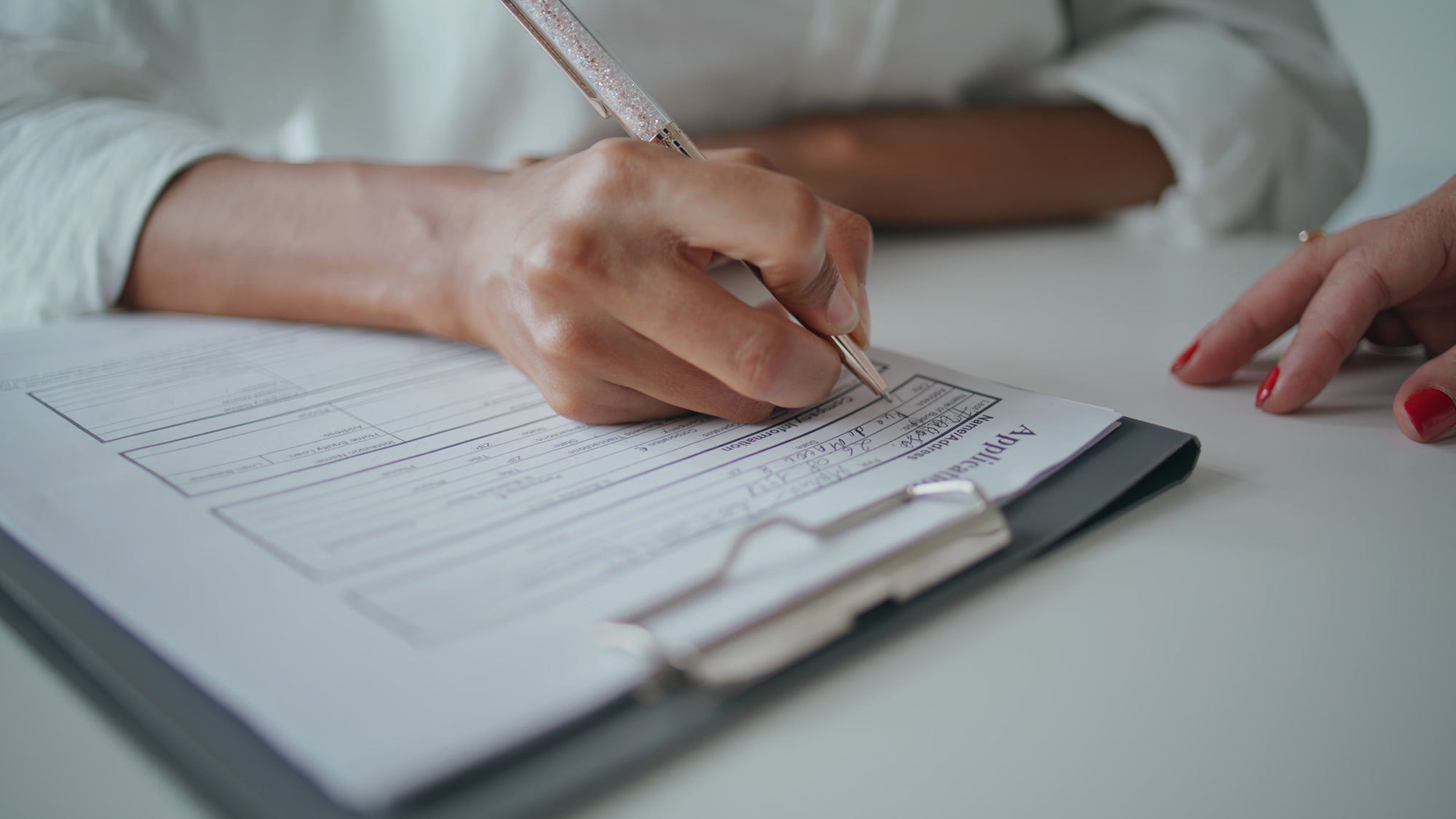 Closeup hands writing application papers on desk. Patient signing insurance form filling personal information at reception. Unknown African American visiting doctor in clinic. Medical system concept.