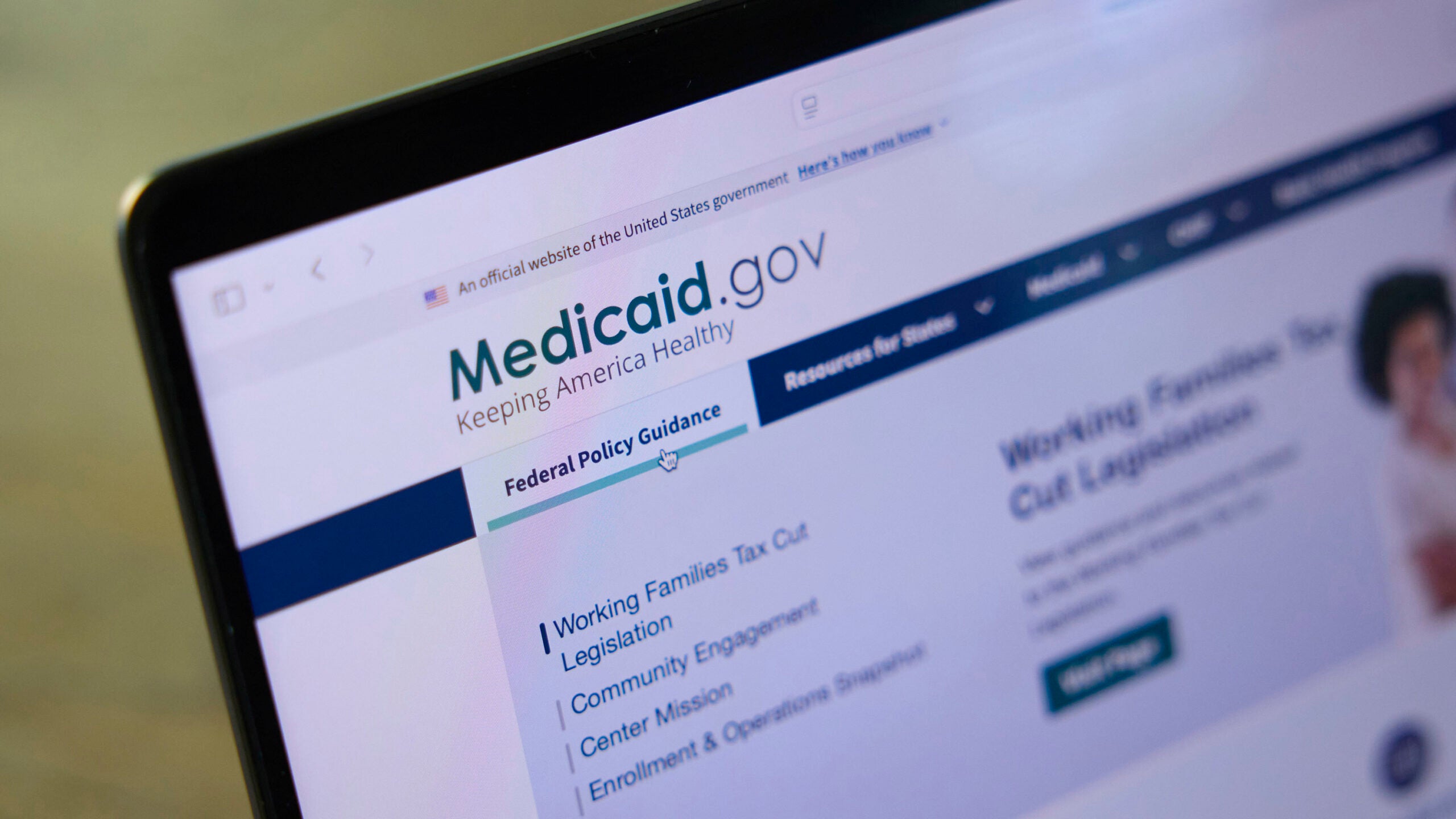 Close-up of a laptop visiting Medicaid.gov and hovering over "Federal Policy Guidance" in its main menu.