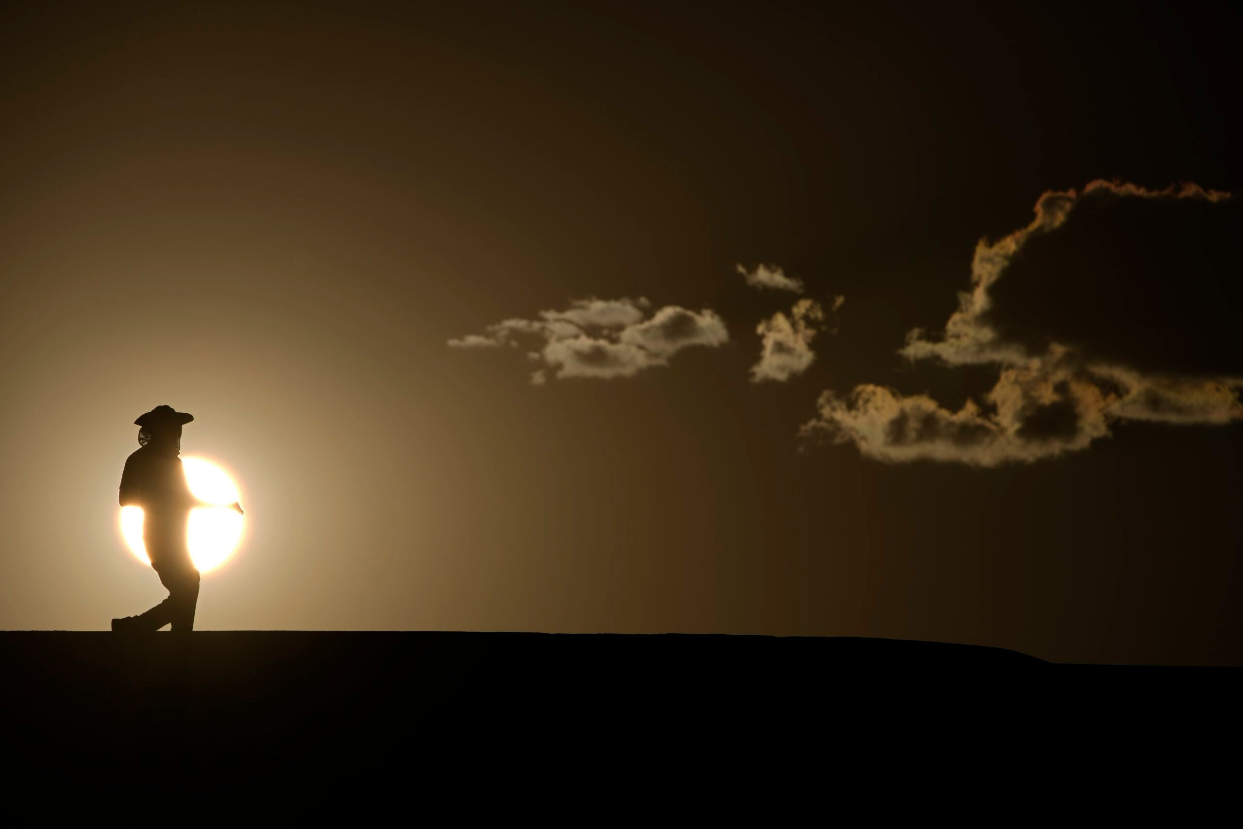 A person walks along a trail as the sun sets, July 16, 2023, in Death Valley National Park, Calif. Their silhouette is pictured against the sun, hanging low in the sky.
