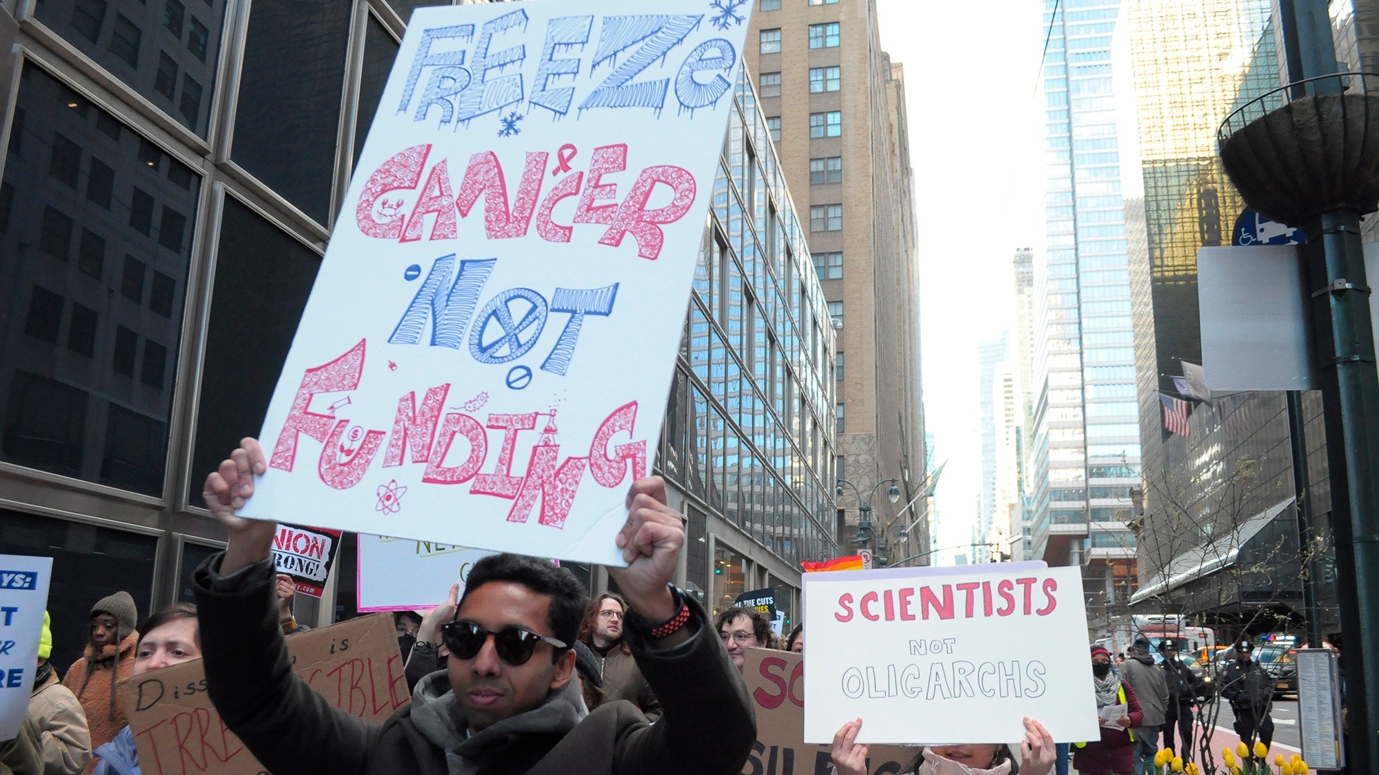 Demonstrators march holding signs at protest against Trump administration's cuts to medical care and research, New York City, April 8, 2025. Photo: Jimin Kim / SOPA Images / Sipa USA via AP Images