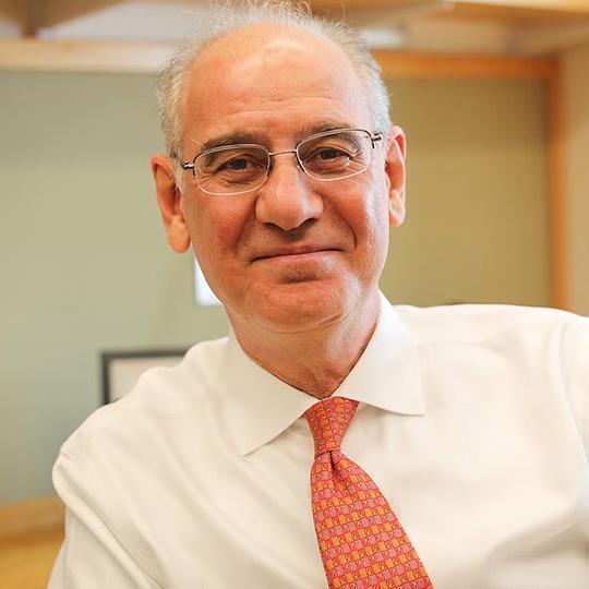 Rifat Atun smiling in an office, wearing a white button down and red tie.