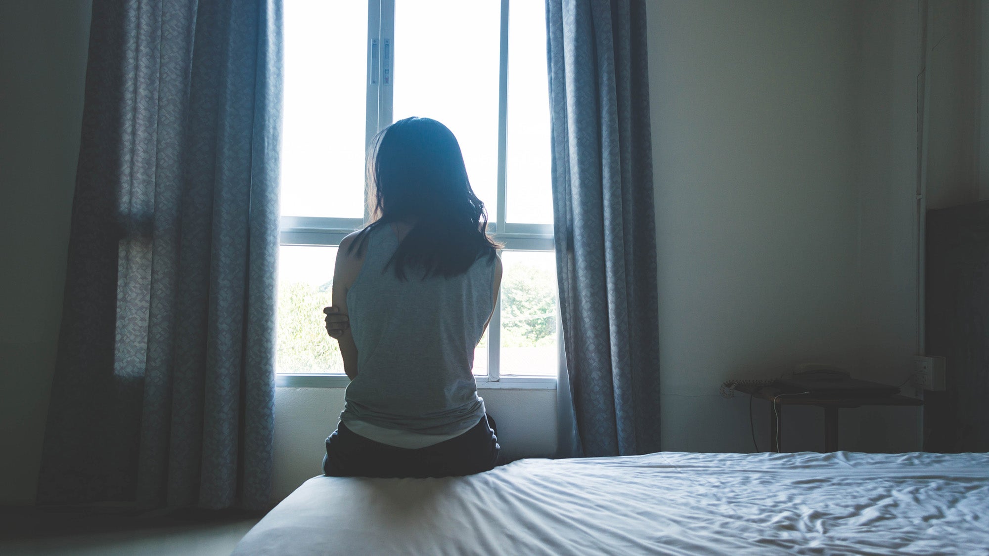 woman sitting on bed in room with light from window