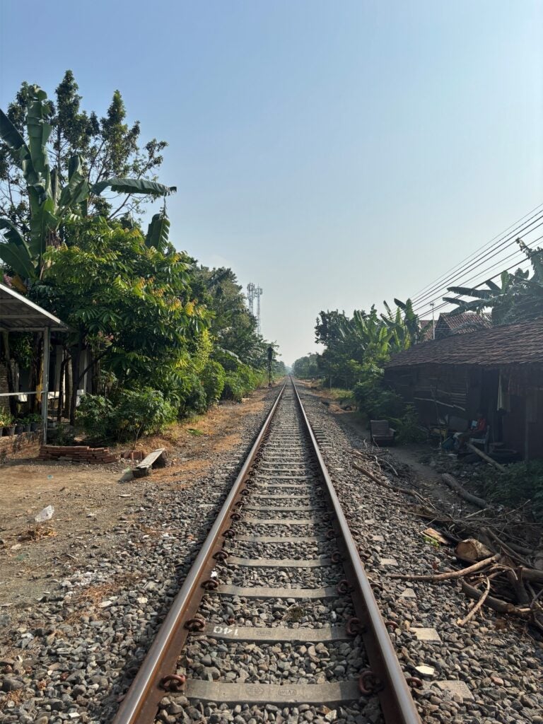 A railway runs through a Javanese village, with homes lining both sides of the tracks.