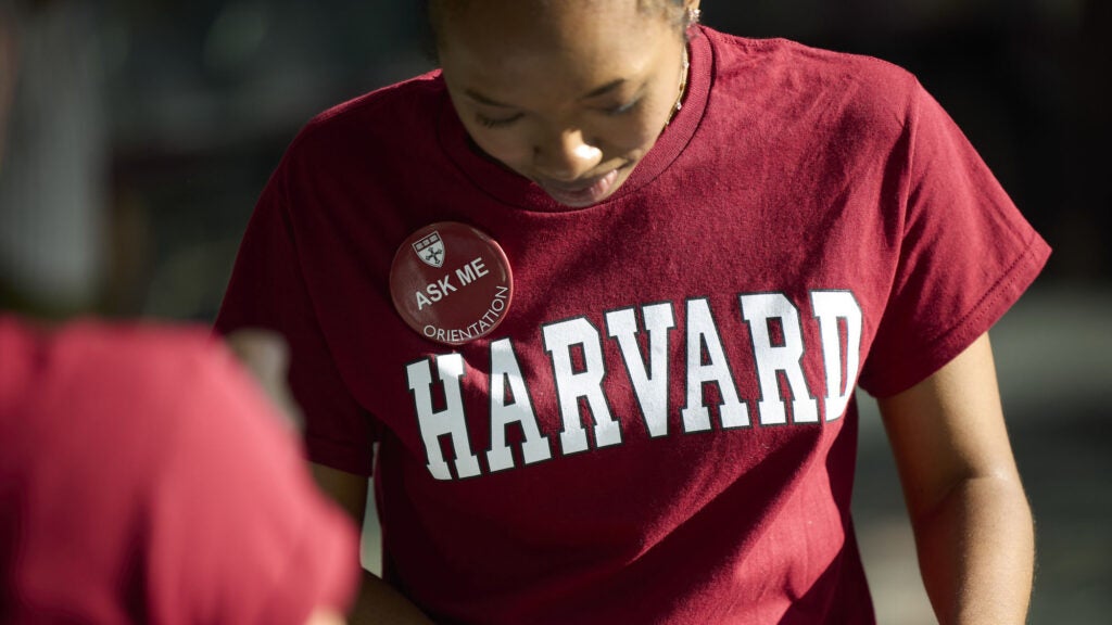 A person wearing a Harvard t-shirt and "Ask Me" button