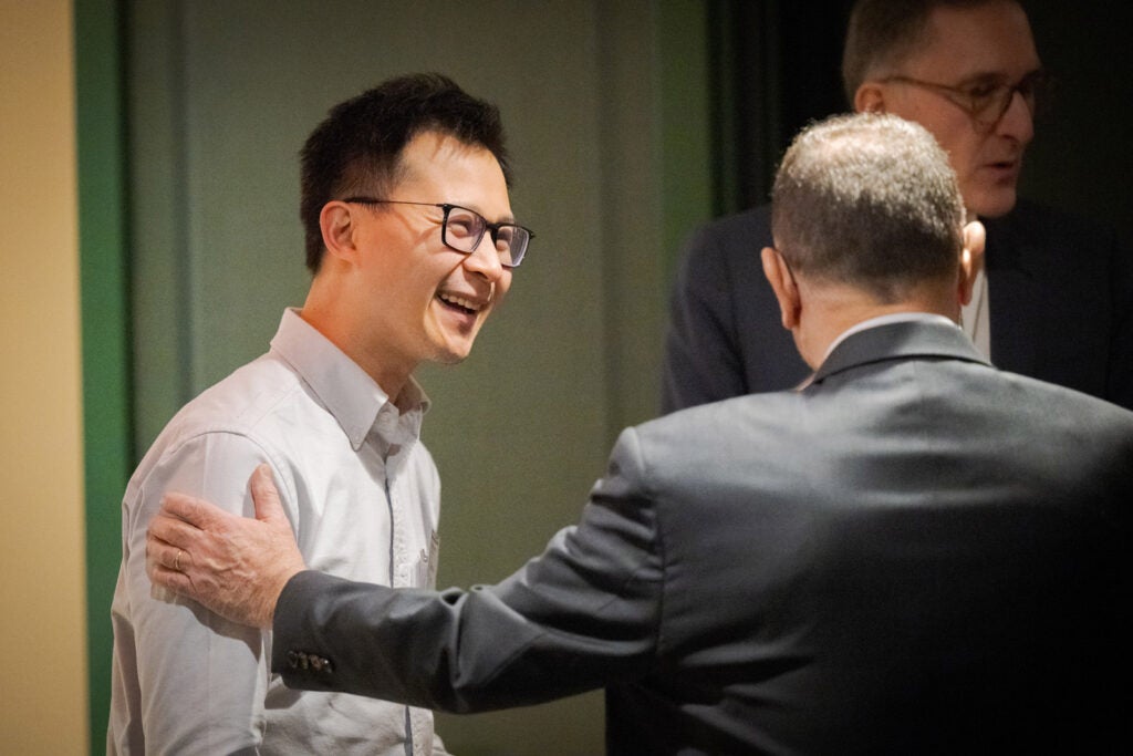 One man laughs while another man touches his shoulder in a welcoming gesture. 