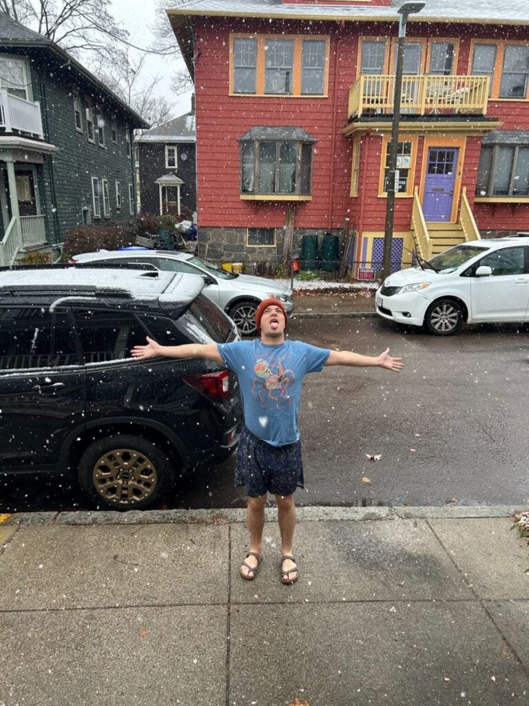 Eric standing on a wet sidewalk, holding his arms out and sticking out his tongue, as snow falls.