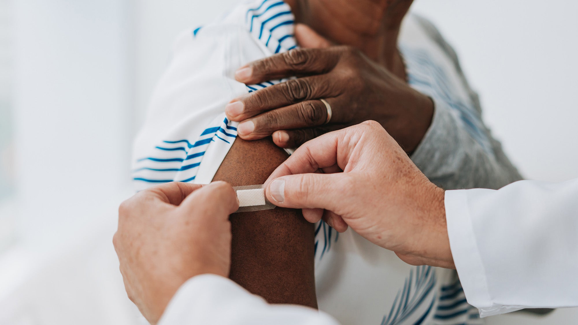 Clinician applying bandage to woman's arm after vaccination