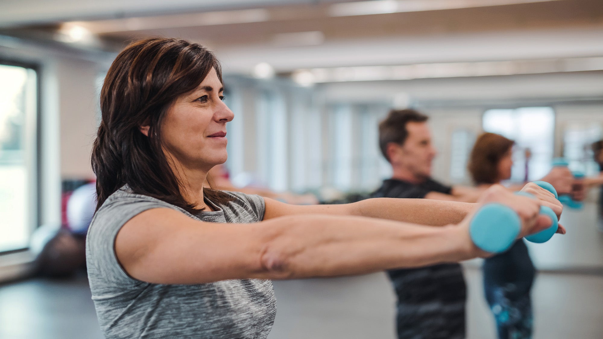 A group of people standing in a gym exercising with dumbbells.