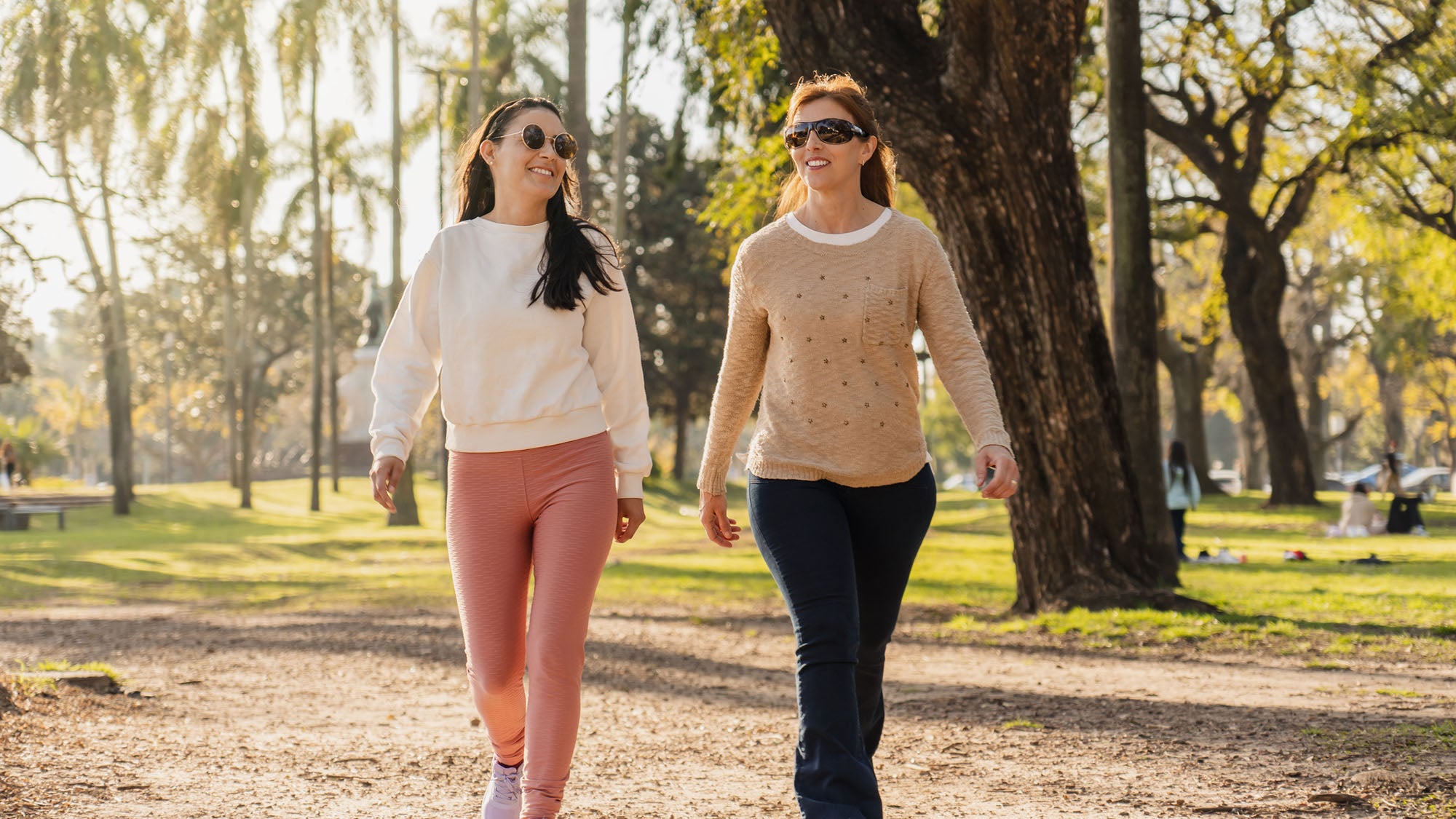 Two women walking on a tree-lined path