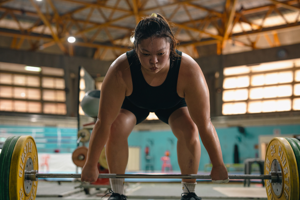 A woman weightlifter prepares to dead lift a barbell with large yellow and green weights on each end.